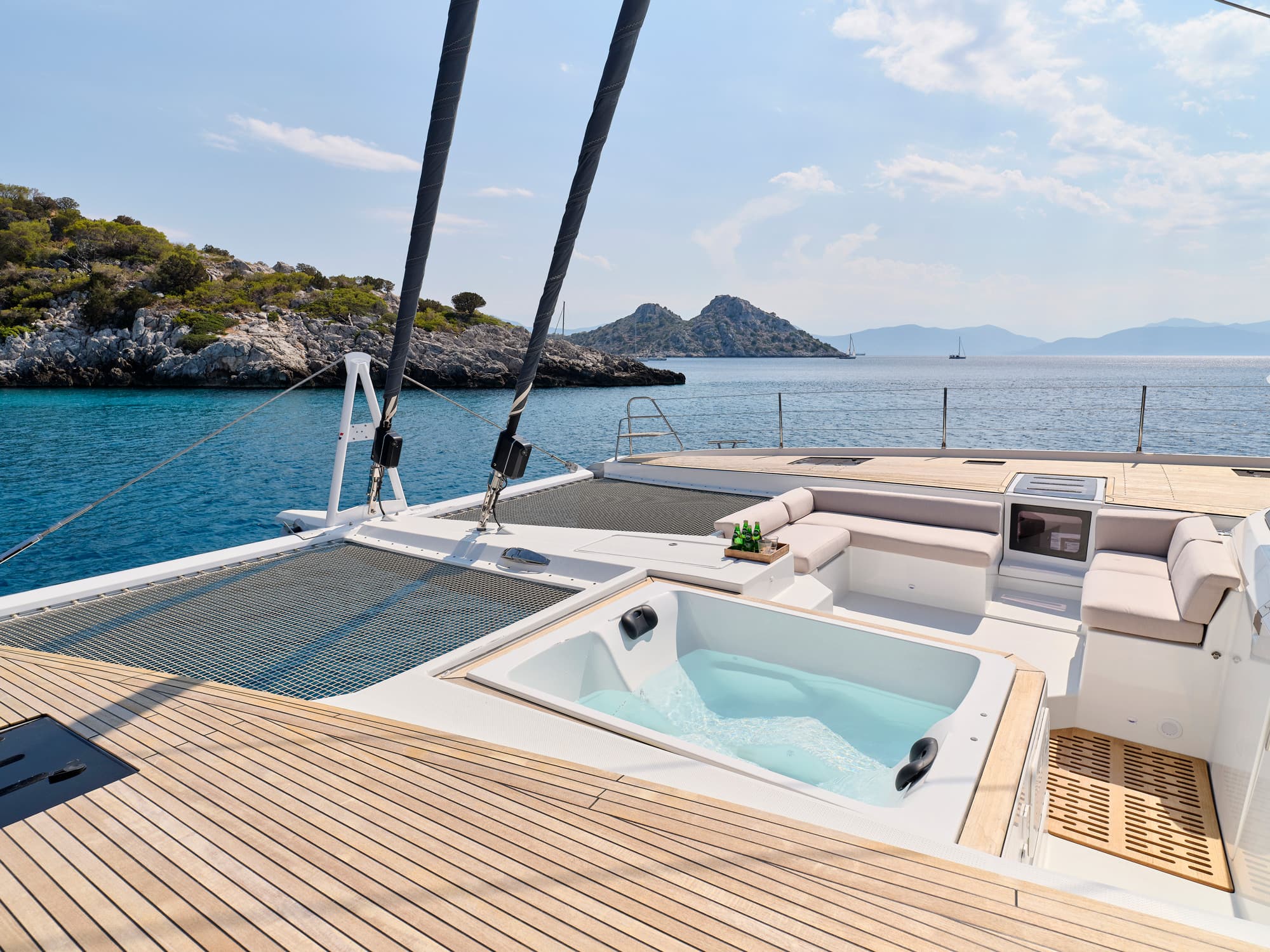 Crewed sailing yacht at anchor in a sheltered bay of the Greek Cyclades, viewed from the foredeck at golden hour